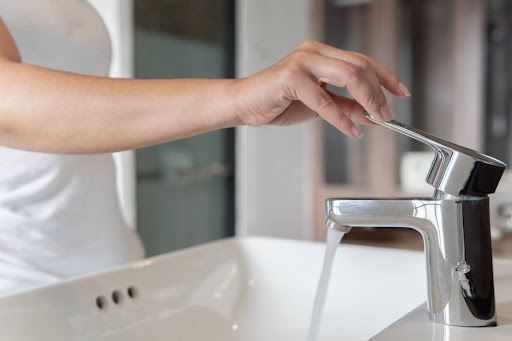 A woman turning on a faucet.