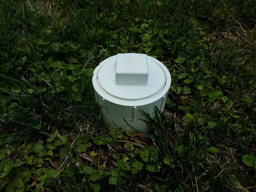 Drain cleanout with cap sticking up a few inches off the ground.