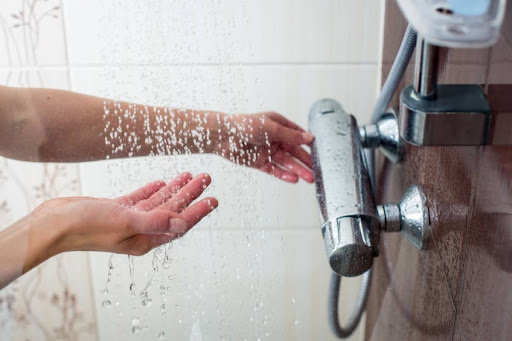 A person testing the water temperature in a shower.